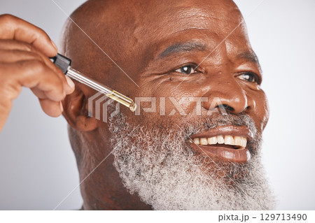 Skincare, wellness and man with a face serum in a studio for a healthy, cosmetic and natural routine. Beauty, cosmetics and African male with a facial oil treatment isolated by a gray background. Skincare, wellness and man with a face serum in a studio for a healthy, cosmetic and natural routine. Beauty, cosmetics and African male with a facial oil treatment isolated by a gray background. 129713490