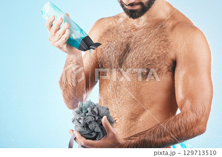 Shower gel, body care and man in a studio for skin hygiene, health and wellness after a shower. Soap, morning routine and male model cleaning or washing his wet body with a sponge by blue background. Shower gel, body care and man in a studio for skin hygiene, health and wellness after a shower. Soap, morning routine and male model cleaning or washing his wet body with a sponge by blue background. 129713510