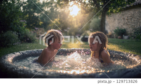two young children joyfully playing, splashing in a small outdoor pool, illuminated by warm glow. It perfectly encapsulates carefree spirit of summer, childhood fun, refreshing outdoor activities 129713826