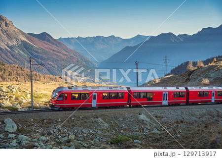 Red Bernina Express train traveling through a high alpine valley Red Bernina Express train traveling through a high alpine valley 129713917