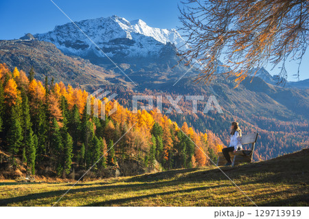 Woman sitting on a bench in autumn forest in the Swiss Alps Woman sitting on a bench in autumn forest in the Swiss Alps 129713919