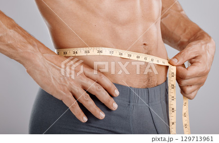 Man, body and tape measure on waist in studio on gray background. Health, fitness and male model with measuring tape for abdomen to track exercise training results, muscle goals or weight loss target Man, body and tape measure on waist in studio on gray background. Health, fitness and male model with measuring tape for abdomen to track exercise training results, muscle goals or weight loss target 129713961