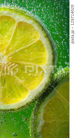 Macro shot of vibrant green lime slices submerged in sparkling water, covered in effervescent bubbles. Perfect for illustrating freshness, carbonation, and refreshing drinks 129714020