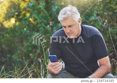 Fitness, phone or old man streaming a podcast, radio music or motivational audio for running exercise or workout. Wellness, relaxing or senior person listening to a song in headphones in nature park 129714185