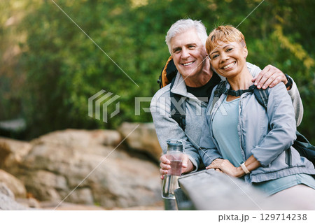 Nature, hiking and portrait of a senior couple relaxing while walking in a forest for exercise. Love, happy and elderly people with a smile sitting to rest while trekking together in the woods. 129714238