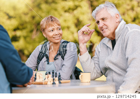 Senior couple playing chess in nature after a wellness, fresh air and health walk in a garden. Happy, smile and elderly people talking, bonding and enjoying a board game together in a green park. 129714245
