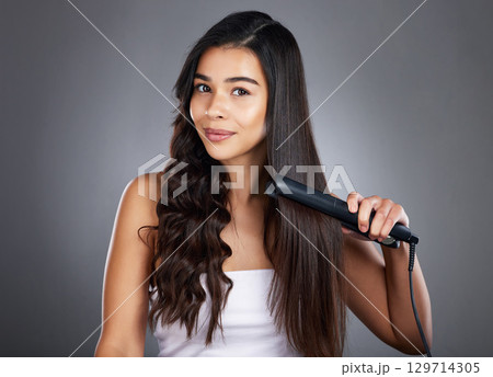Portrait, woman and hair straightener for care, natural beauty or treatment on grey studio background. Female, girl and salon equipment for luxury, ironing hair style and grooming routine for styling 129714305