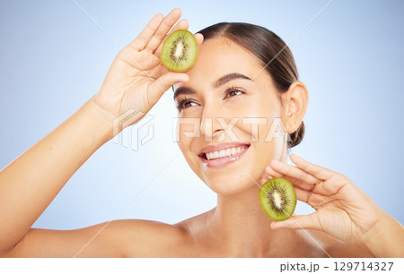 Beauty, kiwi and woman with face and smile, skincare and organic, vegan cosmetic care for healthy skin. Microblading, natural cosmetics and hands frame with fruit, facial and glow on blue background. 129714327