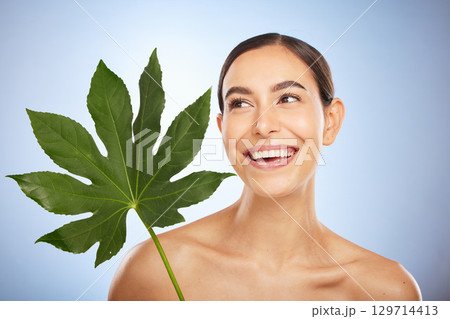 Woman, skincare and plant leaf in studio for self care beauty, wellness and smile by blue background. Model, happy and monstera leaves for natural cosmetic, radiant skin glow or aesthetic by backdrop 129714413