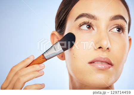 Woman, face and thinking with makeup brush for skincare beauty, luxury skin wellness and cosmetics dermatology in studio. Facial care, product application or spa vision aesthetic in blue background 129714459
