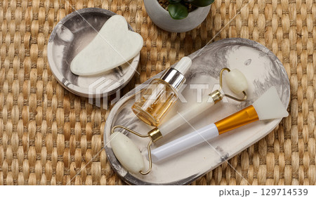 Facial care items lying on an oval tray. A bottle with a pipette and two facial massage rollers Facial care items lying on an oval tray. A bottle with a pipette and two facial massage rollers 129714539