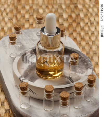 A bottle with a pipette surrounded by small empty bottles with corks. The objects are arranged on a marble tray, a wicker background A bottle with a pipette surrounded by small empty bottles with corks. The objects are arranged on a marble tray, a wicker background 129714540