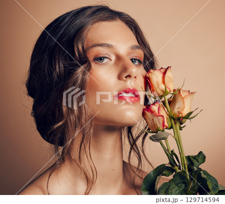 Beauty, flowers and face of woman in studio for wellness, fashion and skincare on brown background. Makeup, cosmetics and female model with roses for beauty salon, natural self care and spa aesthetic 129714594