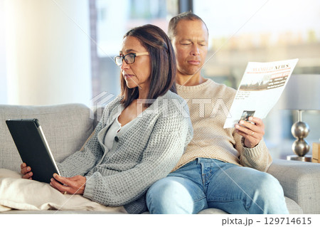 Tablet, newspaper and couple relax on sofa, bonding and streaming video at home. Technology, love and mature man reading news and woman with touchscreen on social media or internet browsing in house. 129714615