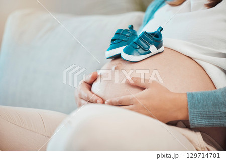 Pregnant, belly and baby shoes on sofa for woman, future mother or ready for kids, children or motherhood. Woman, pregnancy or kid sneakers for dream, vision or preparation at family home for child 129714701