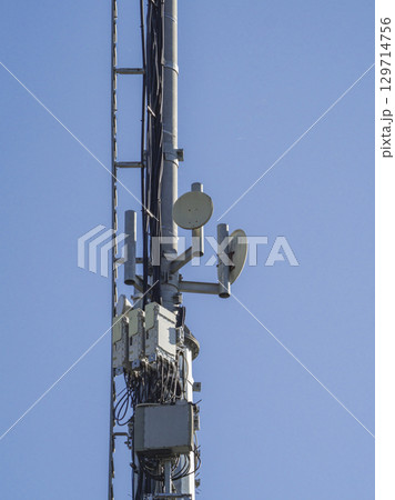 Telecommunication tower against a clear blue sky, featuring antennas, microwave dishes, and electronic equipment, symbolizing modern communication infrastructure 129714756