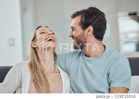 Couple, laughing and home of a woman and man in a living room with love, happiness and care. House, relax and funny joke of a happy couple on a house sofa smile about bonding and marriage together 129715038