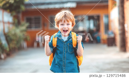 An enthusiastic young schoolboy with a backpack celebrates his return to school with a cheerful and triumphant expression, capturing the joy and excitement of a new academic adventure 129715486