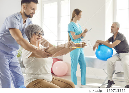 Nurse helping senior smiling woman to do sport stretching exercises with rubber band 129715553