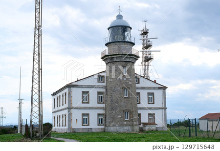 A beautiful historic lighthouse building in Asturias made of stone, standing majestically on a green hill with a grassy lawn. 129715648
