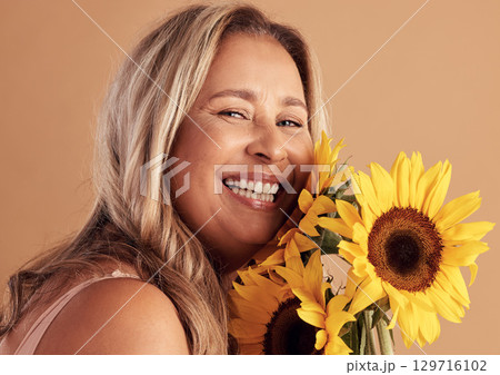 Mature woman and beauty portrait with flower bouquet and happy smile for natural skincare campaign. Wellness, cosmetics and healthy skin of latino person with sunflowers on beige studio background. Mature woman and beauty portrait with flower bouquet and happy smile for natural skincare campaign. Wellness, cosmetics and healthy skin of latino person with sunflowers on beige studio background. 129716102