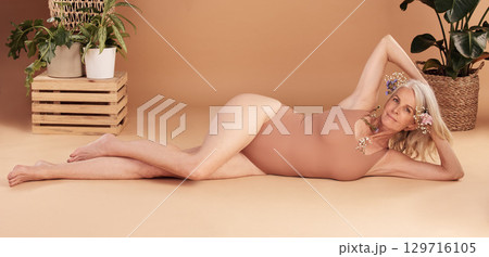 Beauty, body positivity and natural with a senior woman lying on the floor of a studio on a beige background. Portrait, skin and underwear with a mature model female posing for luxury or wellness Beauty, body positivity and natural with a senior woman lying on the floor of a studio on a beige background. Portrait, skin and underwear with a mature model female posing for luxury or wellness 129716105