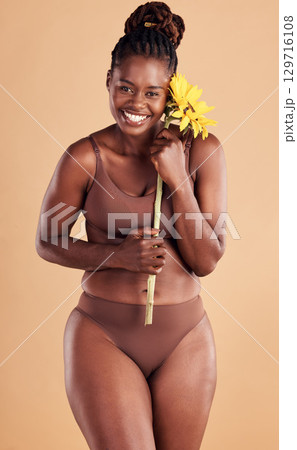 Beauty, wellness and portrait of black woman with sunflower in studio for skincare, self care and self love. Health, cosmetics and plus size girl with flower for natural beauty products and makeup Beauty, wellness and portrait of black woman with sunflower in studio for skincare, self care and self love. Health, cosmetics and plus size girl with flower for natural beauty products and makeup 129716108