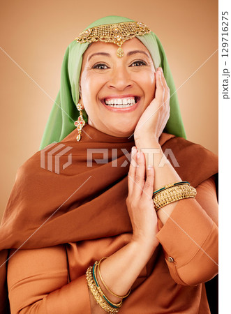 Portrait, face and skincare with a muslim woman in studio on a brown background for culture or tradition. Happy, smile and beauty with an islamic female posing to promote natural care or heritage 129716275