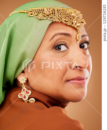 Mature muslim woman, face or fashion hijab on studio background with traditional jewellery, religion jewelry or trendy accessory. Zoom, portrait or middle aged Islamic model in stylish hijab earrings 129716285