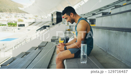 Athlete, man and relax with phone at stadium for social media, fitness app and event agenda. Male person, rest and mobile for texting contact, sports progress results and information for tournament 129716487