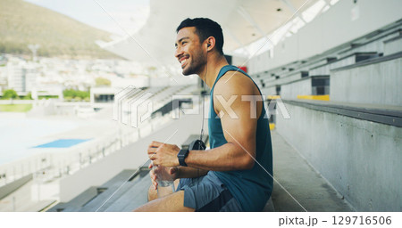 Stadium, man and earphones with water bottle for fitness, hydration and running break. Outdoor, athlete person and thinking with smile for training podcast, exercise and music for workout rest Stadium, man and earphones with water bottle for fitness, hydration and running break. Outdoor, athlete person and thinking with smile for training podcast, exercise and music for workout rest 129716506
