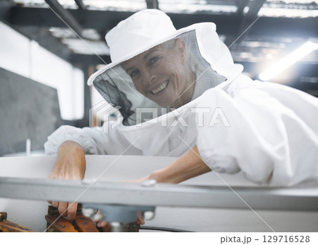Woman, beekeeper suit and honey production, manufacturing and process in workshop, factory or warehouse. Smile of happy bee farmer for beehive inspection harvest and maintenance of small business 129716528