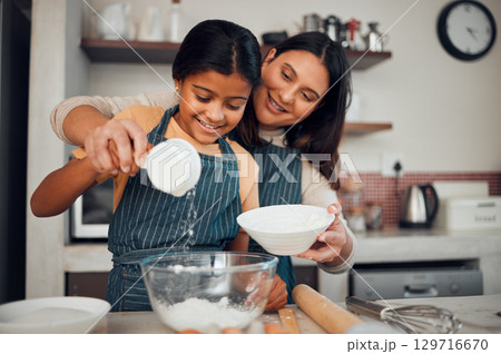 Baking, children and kitchen with a mother and daughter learning about cooking or food in their home together. Family, love and bonding with an indian woman teaching her female child how to bake Baking, children and kitchen with a mother and daughter learning about cooking or food in their home together. Family, love and bonding with an indian woman teaching her female child how to bake 129716670