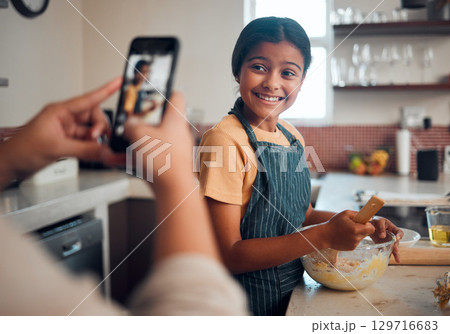 Baking, girl and phone picture of a child cooking in home kitchen with a proud smile about learning. Happy, cooking development and kid in a house helping to make cookies with mom and mobile photo 129716683