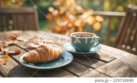 Golden Flaky Croissant and a Warm Cup of Coffee on a Sunny Outdoor Patio Table, Capturing the Cozy and Relaxing Mood of an Autumn Morning 129716690