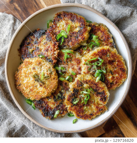 A rustic bowl of crispy, golden-brown cauliflower and quinoa fritters, garnished with fresh green onions. This dish is perfect for illustrating healthy, vegetarian, and gluten-free food options 129716820