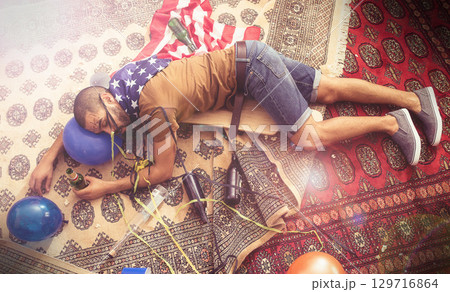 Party, drunk and sleeping man after new years, social or drinking holiday event on a home carpet. Alcohol, celebrate and hangover of a tired person holding a beer bottle drink with addiction problem 129716864
