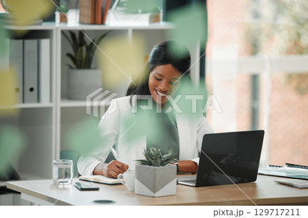 Working, business woman and employee writing at a office desk for financial management. Black woman, web and computer research of a accounting manager busy with schedule and document planning 129717211