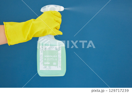 Hand, spray and detergent for cleaning, hygiene or anti bacteria chemical against a blue studio background. Hands of glove spraying liquid bottle for washing, clean sanitary or disinfection on mockup 129717239