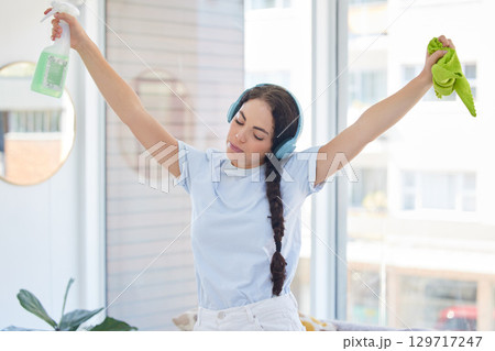 Woman cleaning, dancing and listening to music with headphones while holding cloth and detergent to clean with energy, fun and audio podcast. Female cleaner or maid working in a house or apartment 129717247