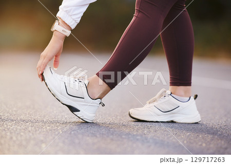 Feet, fitness and stretching woman in street for running, outdoor training and exercise with sneakers, shoes or sports gear marketing. Hand, foot and sports, athlete or runner on road for workout 129717263