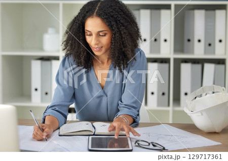 Architecture, engineering and woman with blueprints writing notes on tablet and notebook in office. Strategy, planning and design, black woman architect working on building plans and online documents 129717361