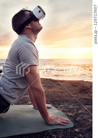 VR, yoga and man stretch on the beach for fitness, flexibility and health and wellness at sunset. Metaverse, ai and futuristic male yogi with a headset and yoga mat for training and ocean pilates 129717607