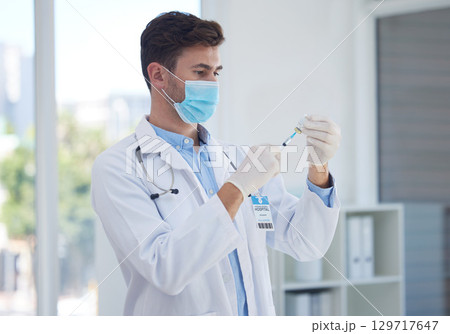 Covid, healthcare and vaccine with a doctor man using a syringe injection for treatment in a hospital. Medical, trust and cure with a male medicine professional ready to inject a corona booster shot 129717647