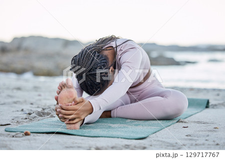 Yoga, fitness and beach with a black woman stretching on an exercise mat for health or wellness in nature. Workout, training and balance with a female yogi doing a warm up by the sea or ocean 129717767
