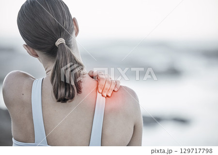 Back, pain and injury with a sports woman holding her shoulder during an exercise workout on the beach. Fitness, health and wellness with a digital CGI or overlay on a female hand outdoor in nature 129717798