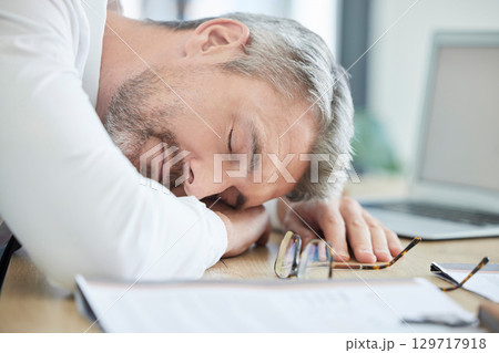 Burnout, sleeping and tired business man at his desk for financial report, audit or tax documents with time management fail or mental health risk. Fatigue, depression and sad businessman in workplace 129717918