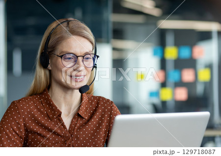 A confident businesswoman in glasses and headset reviewing tasks on a laptop, collaborating remotely. A confident businesswoman in glasses and headset reviewing tasks on a laptop, collaborating remotely. 129718087