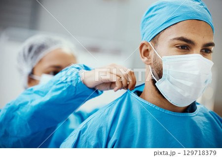 Surgeon, doctor or medical man with nurse helping with clean scrubs and face mask for surgery, healthcare and safety in theatre. Emergency, ppe and operation staff in a hospital for life insurance 129718379