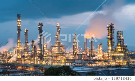 A large industrial oil refinery and chemical plant is illuminated at dusk. Image captures heavy industry, energy production, and complex infrastructure of petrochemical manufacturing and global trade. 129718436